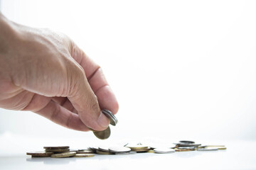 Overexposed image of a young man putting a coin on a group of coin. Selective focus shot. Business concept. Copy space. Isolated on white background