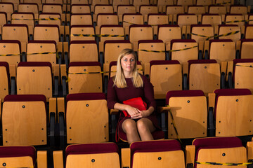 caucasian woman sitting at premiere in empty theatrical hall - obrazy, fototapety, plakaty