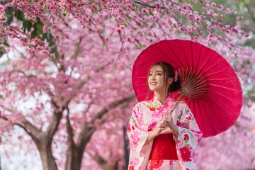 Foto op Plexiglas woman in yukata (kimono dress) holding umbrella and looking sakura flower or cherry blossom blooming in garden © geargodz