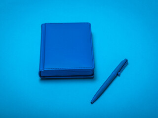 Blue pen and blue notepad on a blue background.