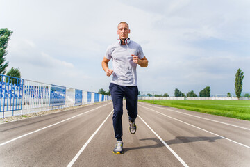 Full length front view on adult caucasian man jogging on the running track - Blonde male athlete in...