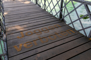 Obraz premium Wooden bridge over the river, on which 'No Jogging' is written in German