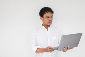 Young Asian man is Angry and hate with laptop. Indonesia Man wear white shirt Isolated grey background.