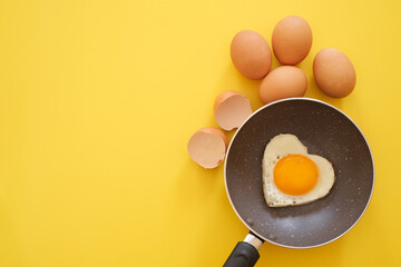 Heart shape fried egg in the pan with egg shell and chicken eggs on yellow background. top view. healthy food  concept. Copy space for text 
