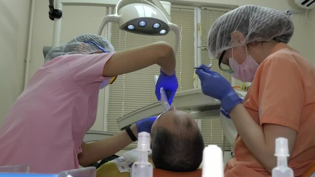 Two young women: a dentist and an assistant are treating a man's teeth.
