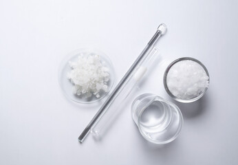 Crystal clear liquid in beaker, Microcrystalline wax in glass container, Flake salt in Chemical Watch Glass placed next to the Stirring Rod and Test tube. Chemicals ingredients on the laboratory table