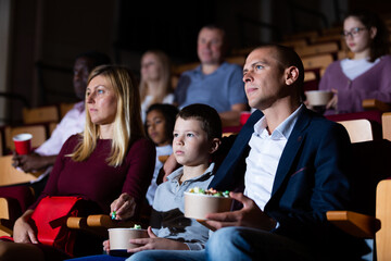 Teenage son watches movie with his parents and eats popcorn in the cinema hall