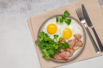 Continental breakfast - fried eggs, bacon and lettuce leaves in a plate on a bright background. Top View