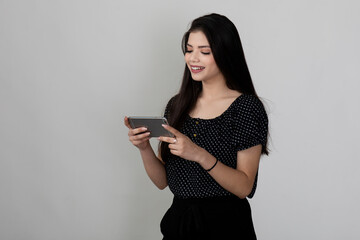Naklejka premium Portrait of pretty young Indian girl standing against white background and holding phone, video conference or video call.