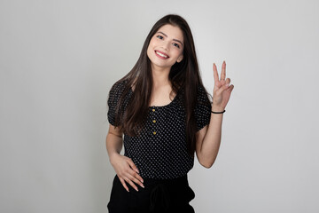 Portrait of pretty young Indian girl raising two fingers to show sing of success and confidence, happy smiling female showing victory symbol.