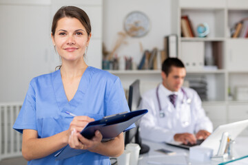 Fototapeta premium Polite female doctor meeting patients in medical office, filling out medical form on clipboard