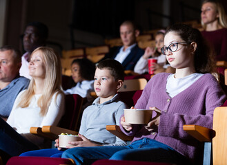 Obraz premium Portrait of teen girl with family sitting in movie theater with popcorn and drinks, watching interesting film