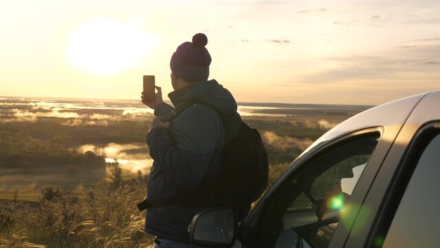 Man traveling by car takes pictures of nature with smartphone. Tourist blogger with modern phone in hand. Driver stopped at campsite in car with modern gadget in his hands. Admire nature from mountain