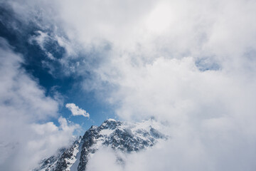 View of mountain peaks and rocks covered with snow around the clouds under the blue sky