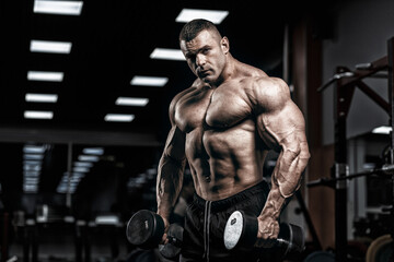 Muscular man bodybuilder training in gym and posing. Fit muscle guy workout with weights and barbell
