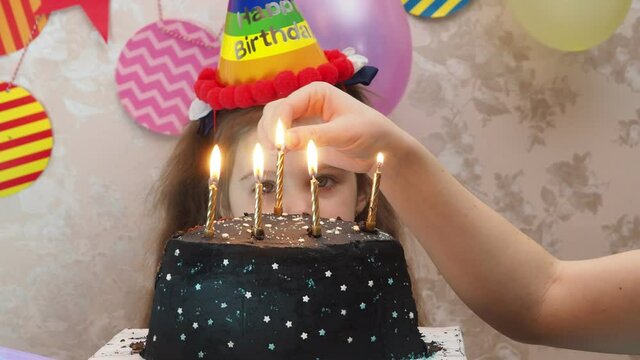 Portrait of little pretty girl with birthday cake a girl in a cap celebrates her birthday, has fun, blows a pipe, blows out the candles on the cake, eats a cake, drinks juice, wears a mask 