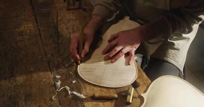 Cinematic shot of master artisan luthier working on creation of handmade fine quality wood violin in his creative workshop. Concept of spiritual instrument, handmade, art, orchestra, artisan, music.