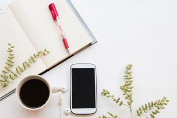 notebook planner ,mobile phone for business work with hot coffee arrangement flat lay style on table white at office desk