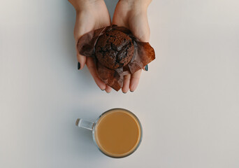 Chocolate muffin in woman's hands and cup of hot coffee next to it. Cocoa and dessert on white...