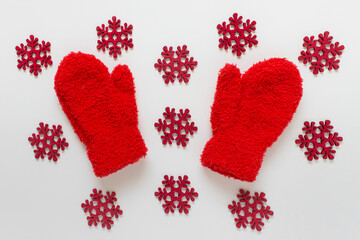 Red fluffy kids mittens with many red wooden snowflakes on white background.