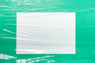 Mockup template with A4 paper sheet and folded uneven celofan food film foil on green paper background.