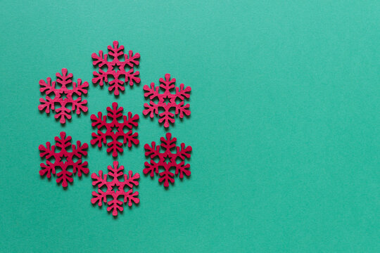 Winter decorative background with red wooden snowflakes arranged as hexagon on green background. Photo with copy blank space.