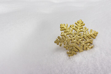Golden snowflake with sparkles laying on real winter snow. Photo with copy blank space.