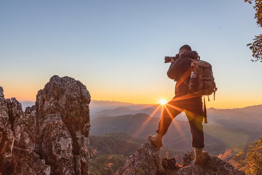 Professional photographer with backpack takes photos on the peak of rocks mountain at sunset,