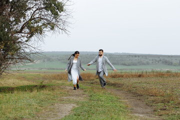 A mischievous couple of newlyweds are running around and having fun in the countryside. Happy moments of the wedding day.
