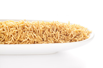 Salty plane Bhujia in a white ceramic oval bowl, made with Chickpeas or gram flour (Besan). Pile of Indian salty snacks (Namkeen), under backlight, side view