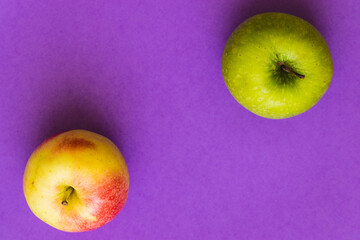 Green apple and yellow-red apple, on a purple background