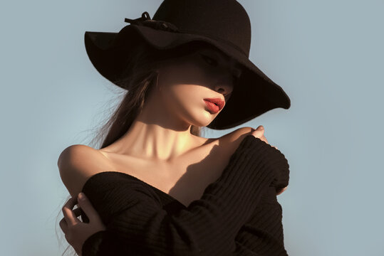 Elegant woman with red lips naked shoulders in black hat. Beauty and fashion portrait.