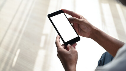 Close up view of young man sitting  with crossed legs in living room and using smart phone.