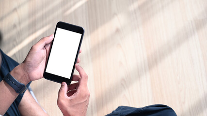 Close up view of young man hands holding mobile phone with blank screen while sitting on wooden floor.