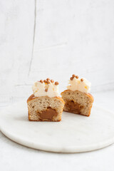 Vanilla cupcake cut filled with salted caramel. Butter cream frosting on the top. Plain background