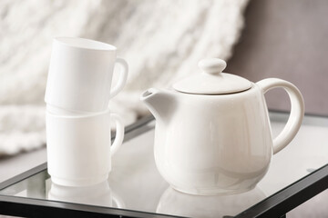 Stylish teapot and cups on table in room