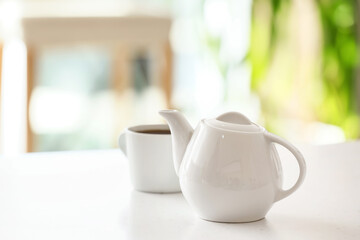 Teapot and cup with tea on light table in room