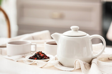 Teapot and dry tea leaves on light table in room