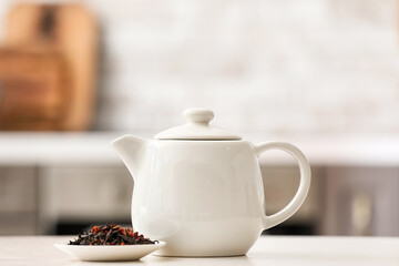 Teapot and dry tea leaves on light table in room