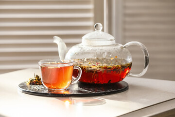 Stylish teapot and cup with tea on light table in room