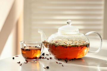 Stylish teapot and cup with tea on light table in room
