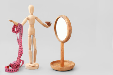 Wooden mannequin with measuring tape  and mirror on light background