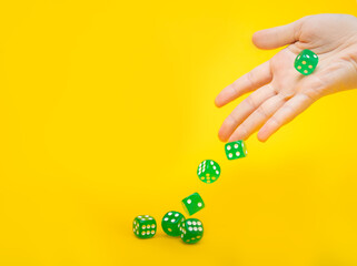 A lot of green dice fall from the hand on a yellow background with space for text: board games, selective focus on the hand, a photo in motion