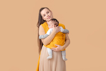 Young mother with little baby in sling on light background