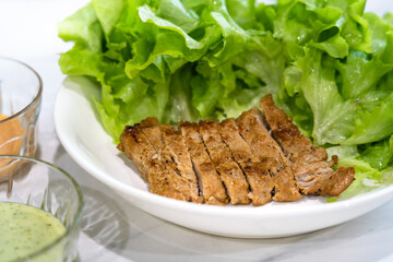 Pork steak with green vegetable and salad cream served in white plate. Food close-up and selective focus at center part of photo.