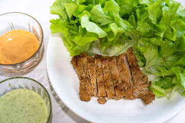 Pork steak with green vegetable and salad cream served in white plate. Food close-up and selective focus at center part of photo.