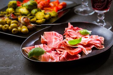 Prosciutto with different appetizers with glass of red wine on black background