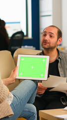 Back view of businesswoman sitting on couch using tablet with green screen talking with colleague while team working on background. Multiethnic coworkers planning project on chroma key display