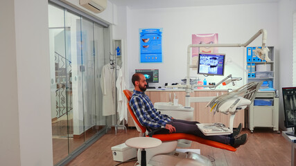 Nurse inviting next patient in stomatology room showing to lie on chair. Dentistry assistant sitting in modernconsultation dental room with man waiting for specialist dentist doctor.