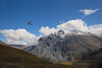 High mountain. covered with snow. The helicopter flies against the blue sky.